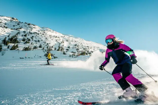 Narciarka w różowym kasku i goglach szaleje na stoku Kasprowego Wierchu, zostawiając za sobą chmurę śniegu.