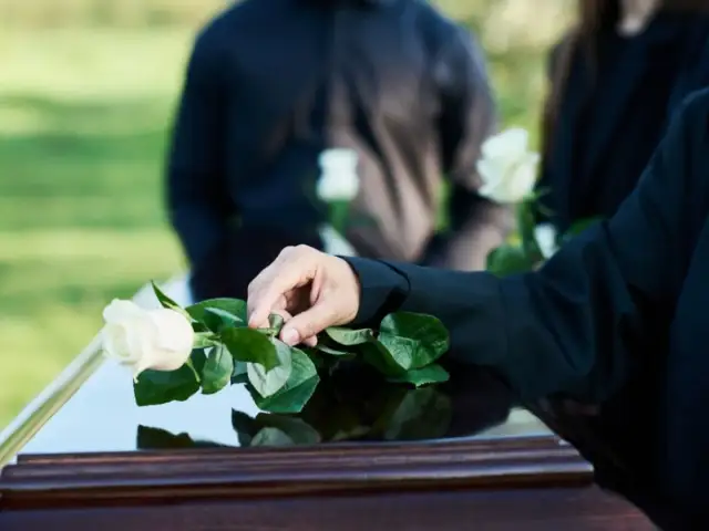Dłoń kładzie białą różę na trumnie. Czy zmarły widzi swój pogrzeb?
