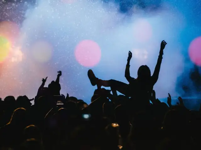 Tłum na jednym z największych festiwali muzycznych na świecie. Kobieta na rękach, ręce w górze, światła sceny.
