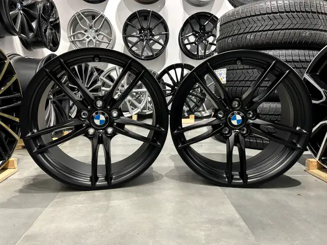 Dwa czarne felgi BMW z logo, idealne do tuningu. W tle inne felgi i opony.