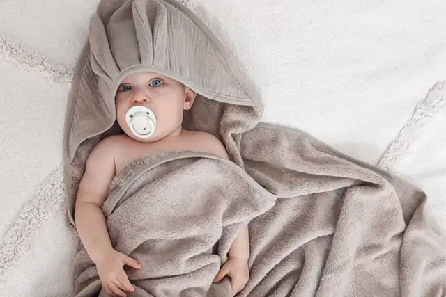 Uroczy niemowlak z niebieskimi oczami i smoczkiem, otulony miękkim, szarym ręcznikiem kąpielowym dla niemowląt.