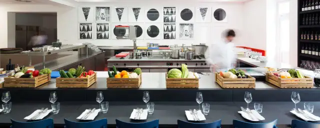 Küchenarbeitsplatz mit frischem Gemüse in Holzkisten und einem Koch im Hintergrund.