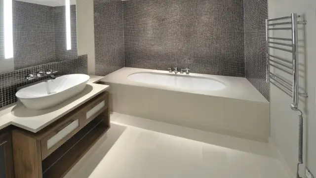 Nowoczesna łazienka z wanną i umywalką na szafce. Blat łazienkowy z konglomeratu tworzy spójną całość z obudową wanny.