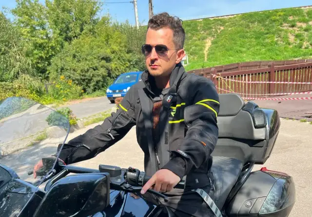 Mężczyzna w okularach przeciwsłonecznych i czarnej kurtce motocyklowej, gotowy na podróż.