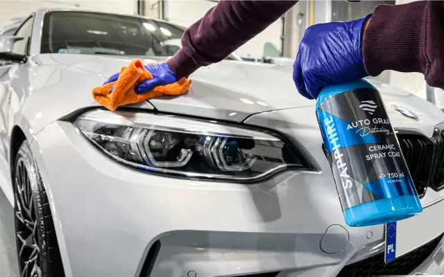 Osoba w niebieskich rękawiczkach aplikuje preparat ceramiczny na biały samochód.