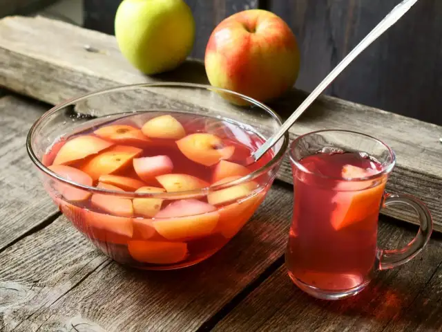 Szklanka i miska pełne pysznego, domowego kompotu z jabłek, obok świeże owoce.