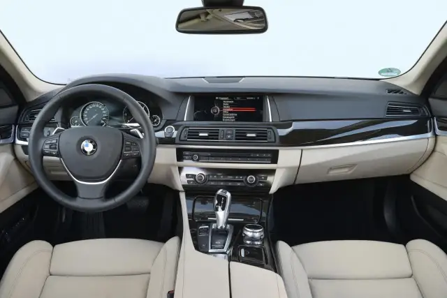 Wnętrze BMW F10 z jasną tapicerką, kierownicą, ekranem multimedialnym i panelem środkowym.