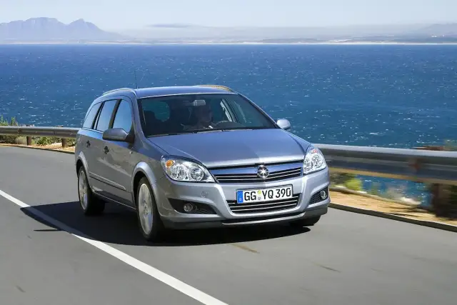 Srebrny Opel Astra H kombi jedzie drogą nad morzem.