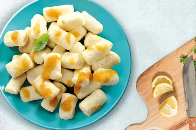 Kluski leniwe z serem i okrasą na talerzu, obok cytryny i noża.