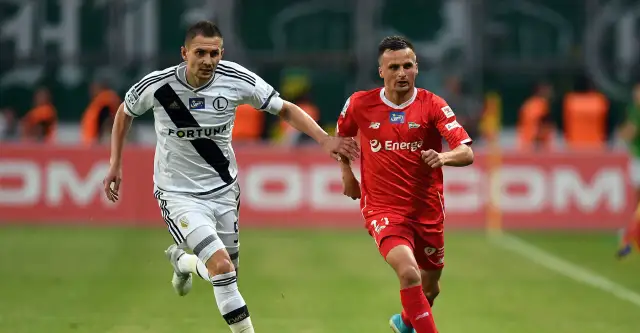 Dwóch piłkarzy w akcji. Jeden w białej koszulce Legii, drugi w czerwonej. Ich gra to dowód na najwyższe zarobki w ekstraklasie.