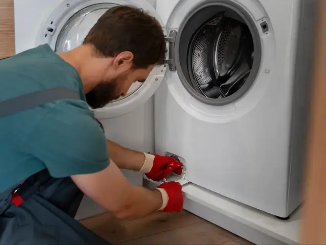 Mężczyzna w czerwonych rękawiczkach otwiera klapkę pralki, przygotowując się do jej czyszczenia. To pierwszy krok, jak odkamienić pralkę.