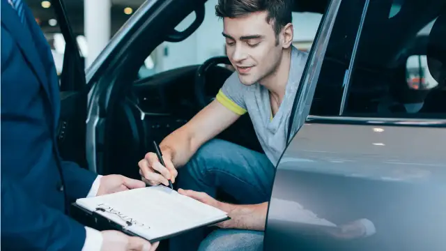 Mężczyzna w samochodzie podpisuje umowę. Chcesz wiedzieć, jak sprawdzić, czy auto jest w leasingu? Dokumenty są kluczem.