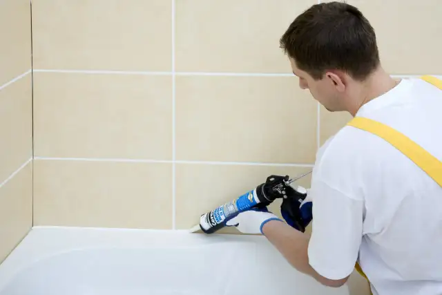 Fachowiec nakłada białą fugę epoksydową Mapei na styku wanny i beżowych płytek, zapewniając estetyczne i szczelne wykończenie.