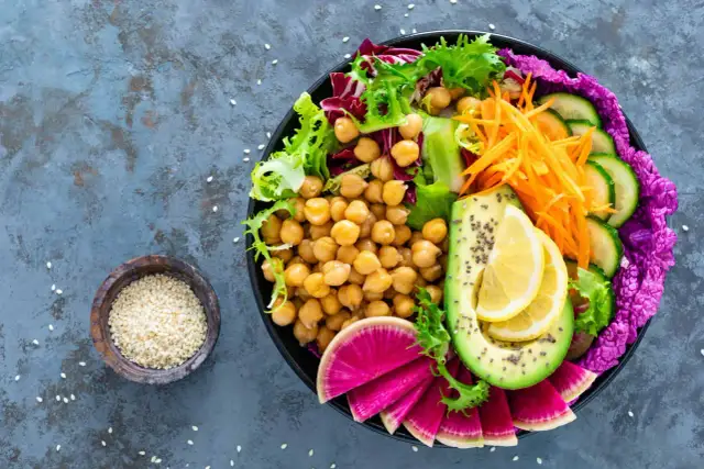 Kolorowa buddha bowl z ciecierzycą, awokado, rzodkiewką, ogórkiem, marchewką i sałatą.