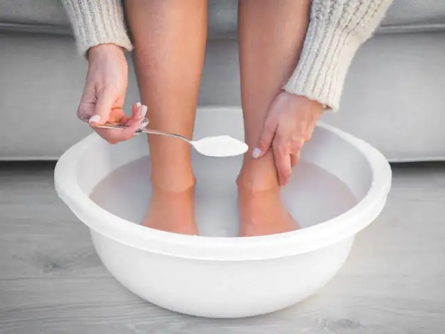 Kobieta dodaje łyżeczkę sody oczyszczonej do miski z wodą, przygotowując domowy zabieg na stopy. Woda z octem na stopy to popularny sposób na ich odświeżenie.