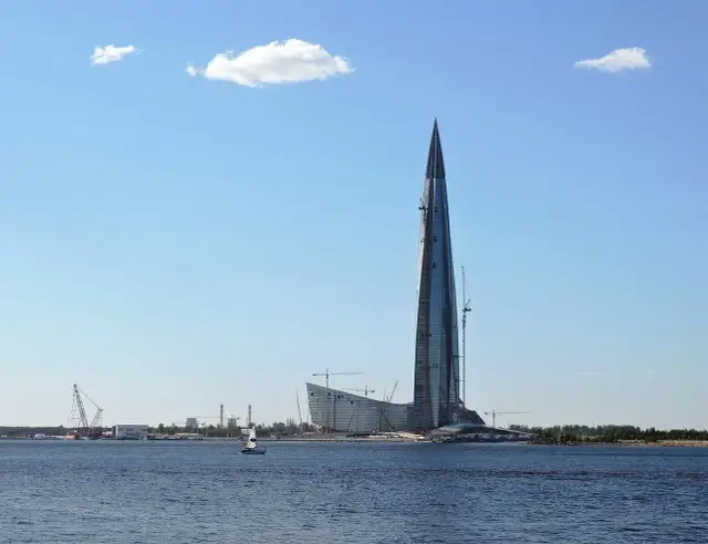 Lakhta Center, najwyższy budynek w Europie, wznosi się nad wodą. W tle widać inne budowy i żaglówkę.