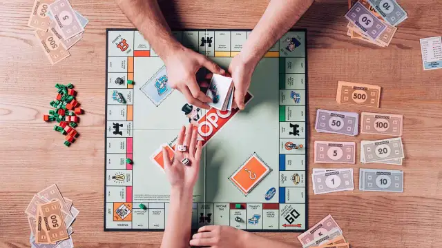 Ręce graczy dzielą pieniądze Monopoly na planszy gry, obok kostek i żetonów.
