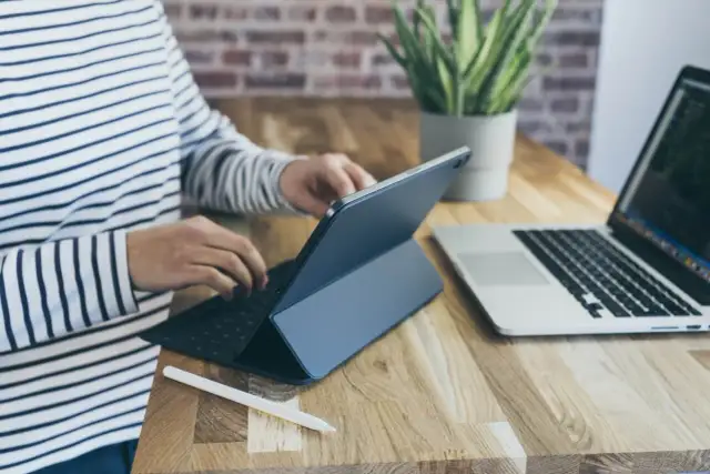 Osoba w paski pracuje na tablecie z klawiaturą, obok laptop. Może sprawdzać kursy walut w getin bank.