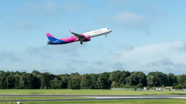 Samolot Wizz Air wznoszący się na tle błękitnego nieba z chmurami.