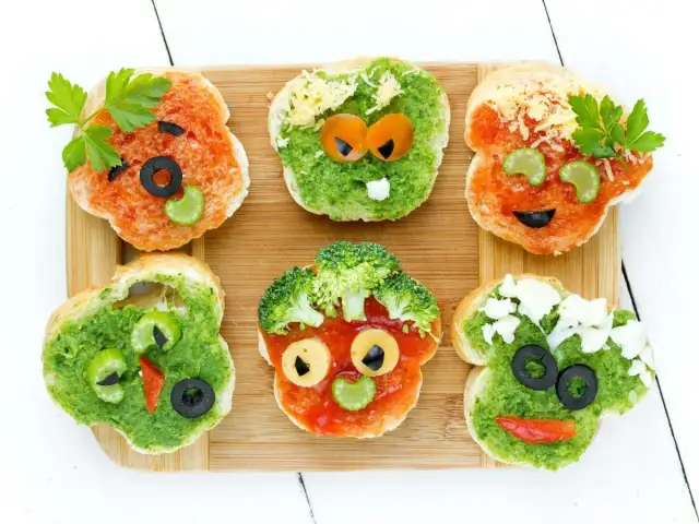 Zabawne przepisy na zdrowe kanapki dla dzieci: bułki w kształcie buziek z warzywami i oliwkami.
