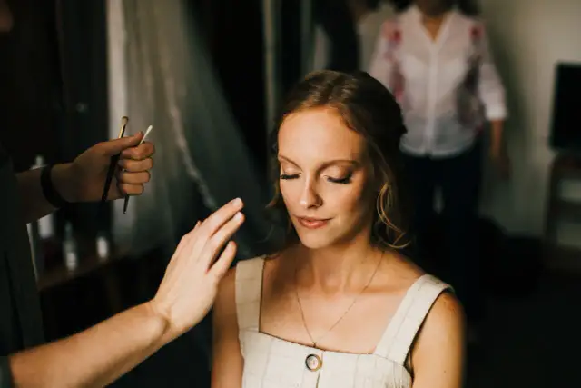 Kobieta z zamkniętymi oczami, której makijaż jest poprawiany przez wizażystkę.