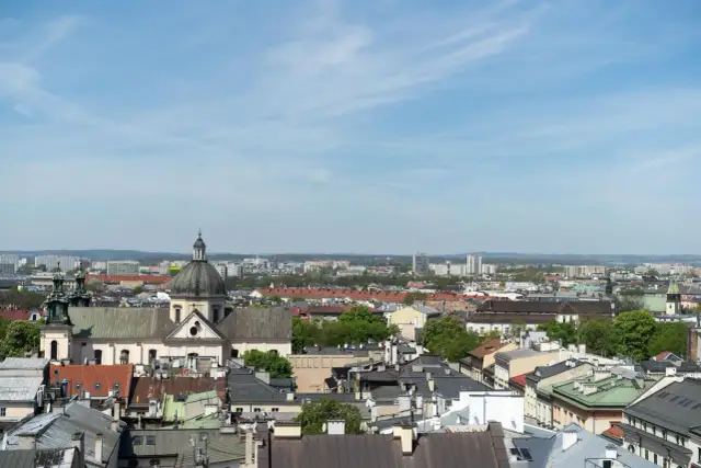 Widok na krakowskie dachy i kościół z kopułą. W tle nowoczesne budynki, które mogą wpływać na ceny mieszkań w Krakowie za m2.