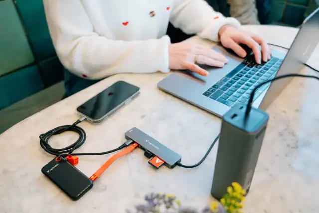 Kobieta pracuje na laptopie, podłączając telefon, dysk zewnętrzny i kartę SD do huba USB 3.2 Gen. 1.