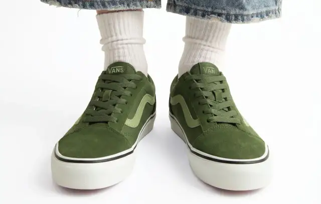 Zielone buty Vans na białym tle, z widocznymi białymi skarpetkami i fragmentem dżinsów.