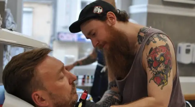 Artysta z tatuażem tygrysa na ramieniu wykonuje nowy wzór. Czy prokurator może mieć tatuaże? Ten artysta z pewnością je ma!