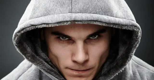 Mężczyzna w szarym kapturze, patrzący intensywnie w obiektyw.