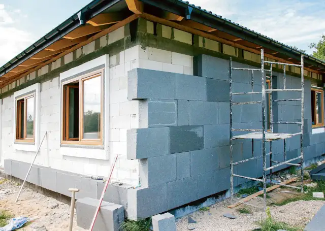 Budowa domu: ściany z białych i szarych pustaków, okna, rusztowanie.