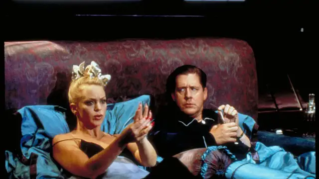 Dama za burtą, w łóżku z mężczyzną, z dramatyczną miną i biżuterią na głowie.