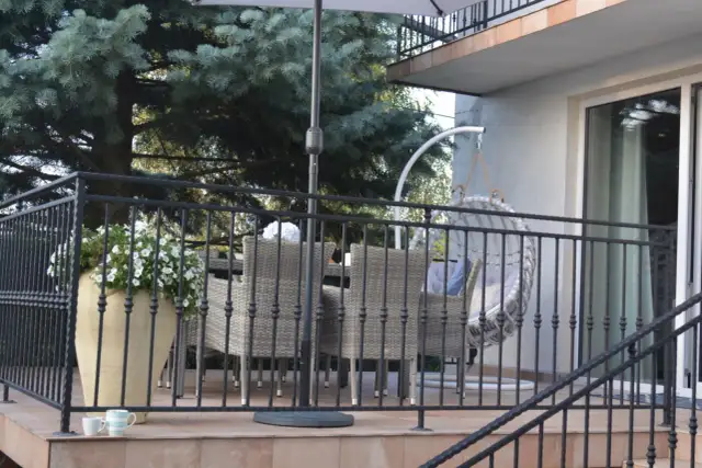 Taras nad garażem inspiracje: rattanowe meble, wiszący fotel i bujna zieleń tworzą przytulną przestrzeń do relaksu.