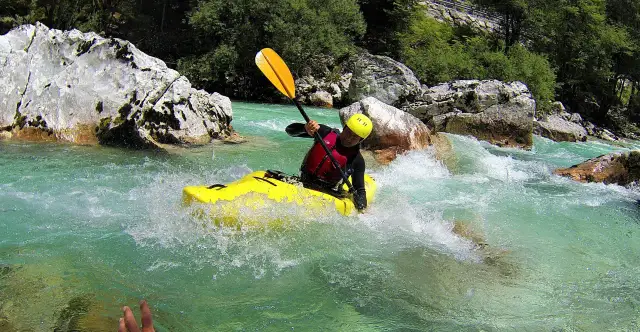 Kajakarz w żółtej łodzi pokonuje bystrą, górską rzekę.
