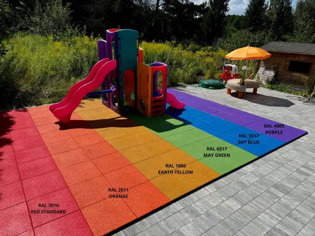 Kolorowy plac zabaw z tęczową nawierzchnią gumową i zjeżdżalnią.