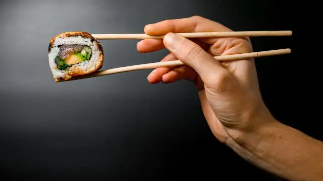 Dłoń trzyma pałeczkami jedno sushi. Zastanawiasz się, ile sushi na osobę będzie idealne na kolację?