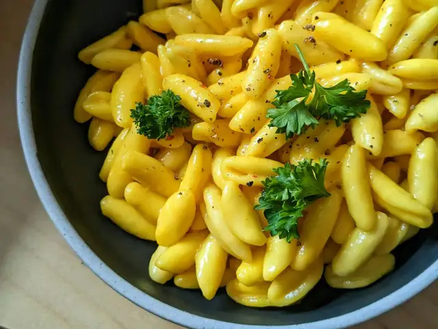 Żółty makaron gnocchi w sosie, udekorowany natką pietruszki i pieprzem, w ciemnej misce.