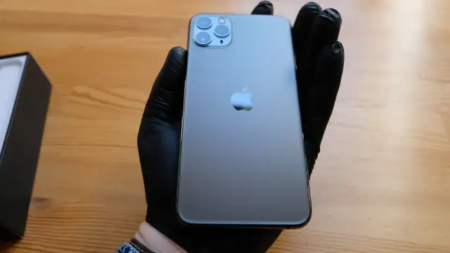 Szary iPhone 11 Pro z potrójnym aparatem, trzymany w czarnej rękawiczce.