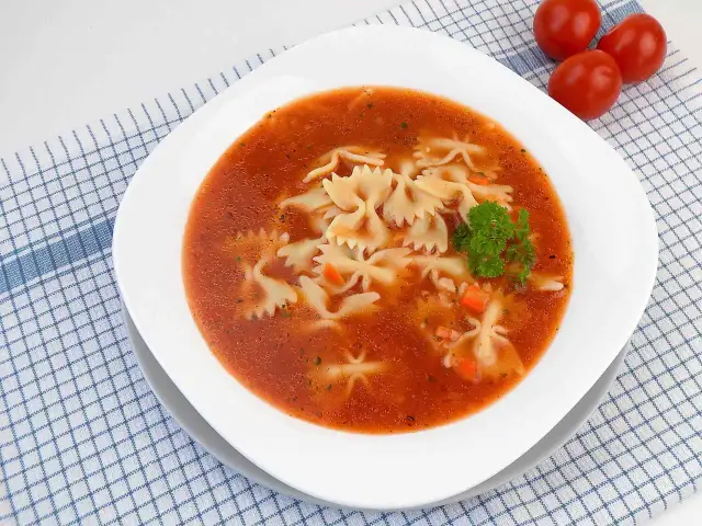 Zupa pomidorowa z makaronem farfalle, marchewką i natką pietruszki na kratkowanym obrusie.