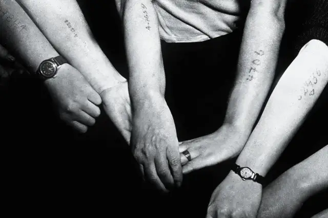 Zbliżenie na ramiona kilku osób z wytatuowanymi numerami i zegarkami.