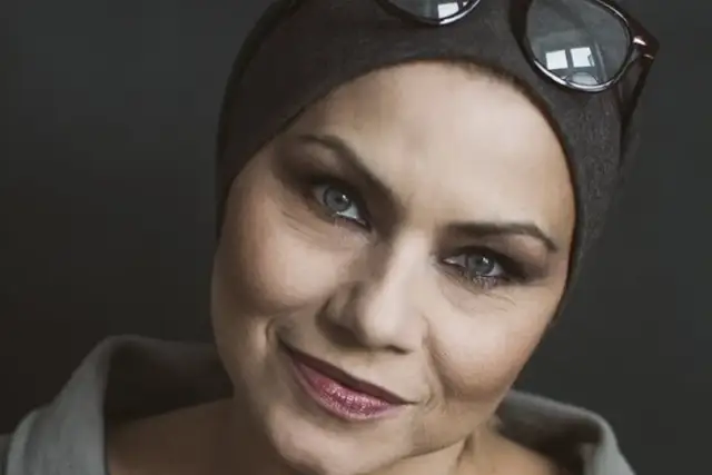 Sylwia Janowicz-Dobrowolska w szarej opasce i okularach na głowie, z wyrazistym makijażem oczu i błyszczącymi ustami.