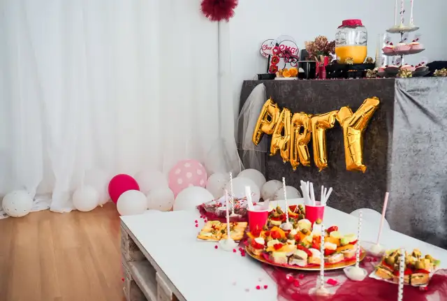 Urocze pomysły na wieczór panieński w domu: złote balony z napisem "PARTY", przekąski i różowe akcenty.