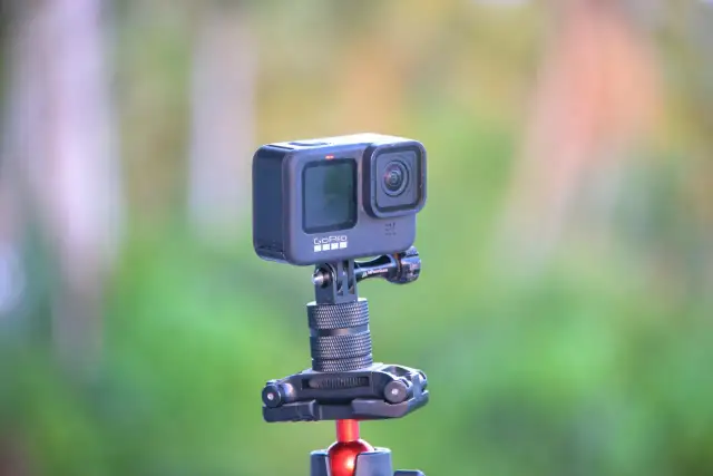 GoPro Hero 10 na statywie z czerwonym mocowaniem, na tle zieleni.