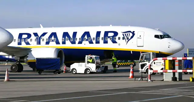 Samolot Ryanair na płycie lotniska z obsługą naziemną i wózkiem bagażowym.