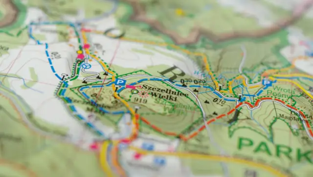 Mapa turystyczna z zaznaczonymi szlakami. Kolory szlaków oznaczają różne trasy piesze i rowerowe, pomagając w nawigacji.