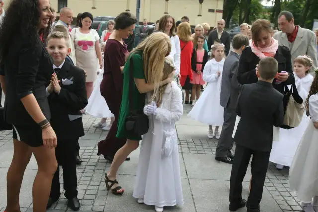Dzieci w strojach komunijnych i dorośli na zewnątrz.