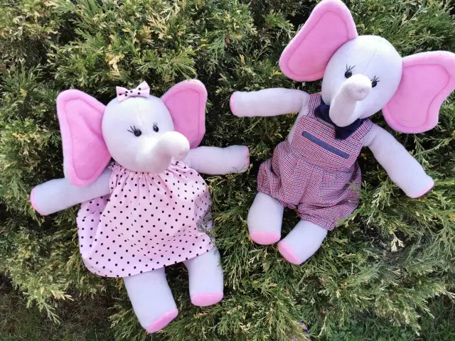 Dwa pluszowe słonie w strojach leżące na zielonych gałązkach.