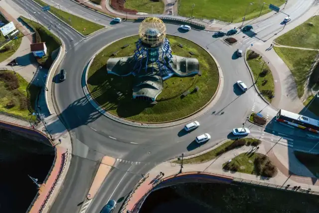 Widok z lotu ptaka na ronda turbinowe i jak jeździć. Samochody i autobus poruszają się po skomplikowanym skrzyżowaniu z centralną rzeźbą.