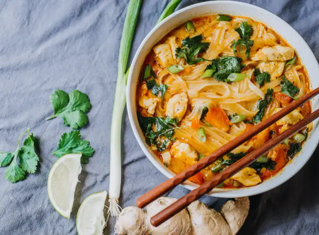 Miseczka z tajską zupą curry z kurczakiem, makaronem ryżowym i warzywami, podana z pałeczkami.