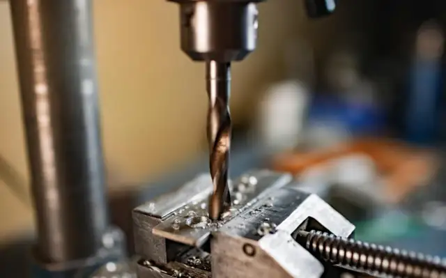 Wiertło wkręca się w metalowy element zamocowany w imadle.